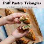 Spinach and Feta Triangles on a baking sheet lined with parchment paper. Hands coming into the frame from the left side holding a triangle cut in half.