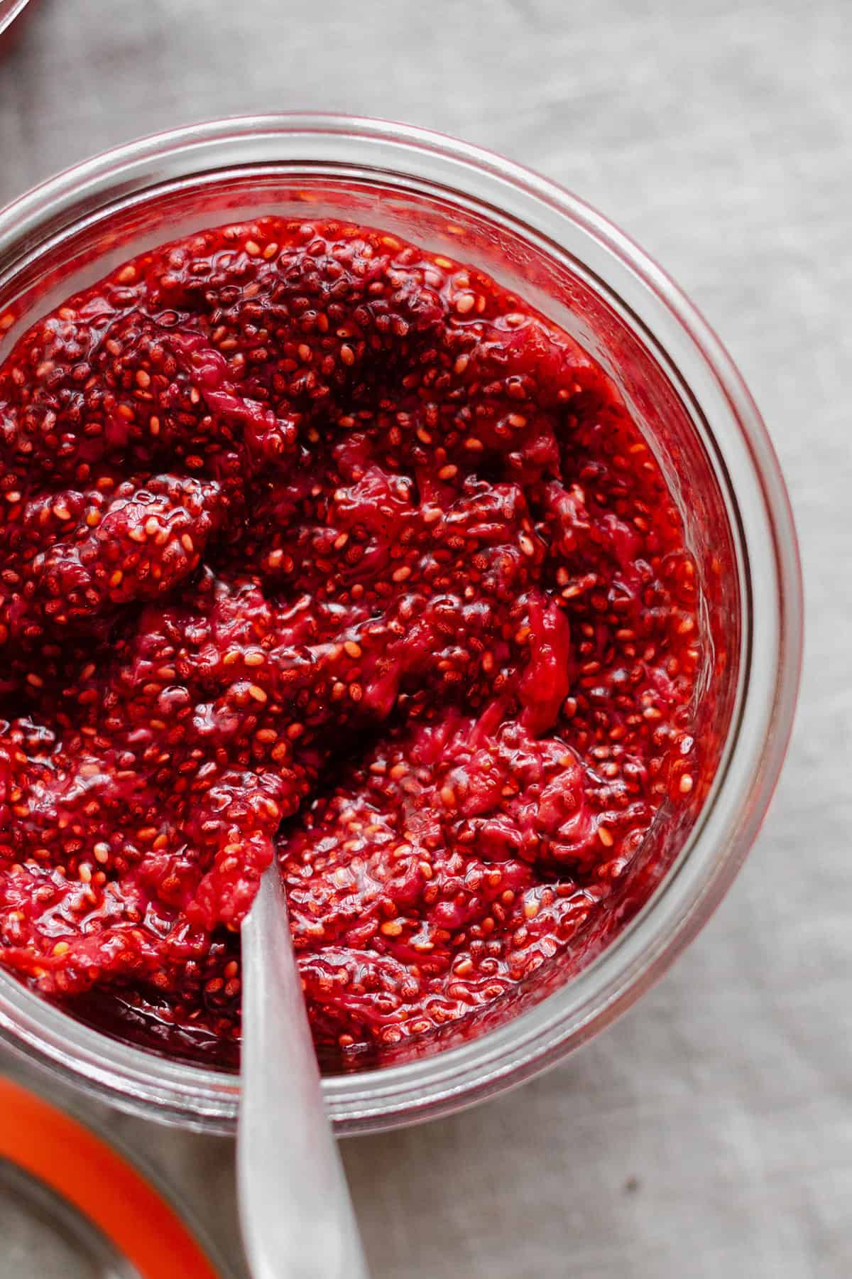 Strawberry Chia Jam in a glass jar with a spoon.