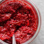 Strawberry Chia Jam in a glass jar with a spoon.