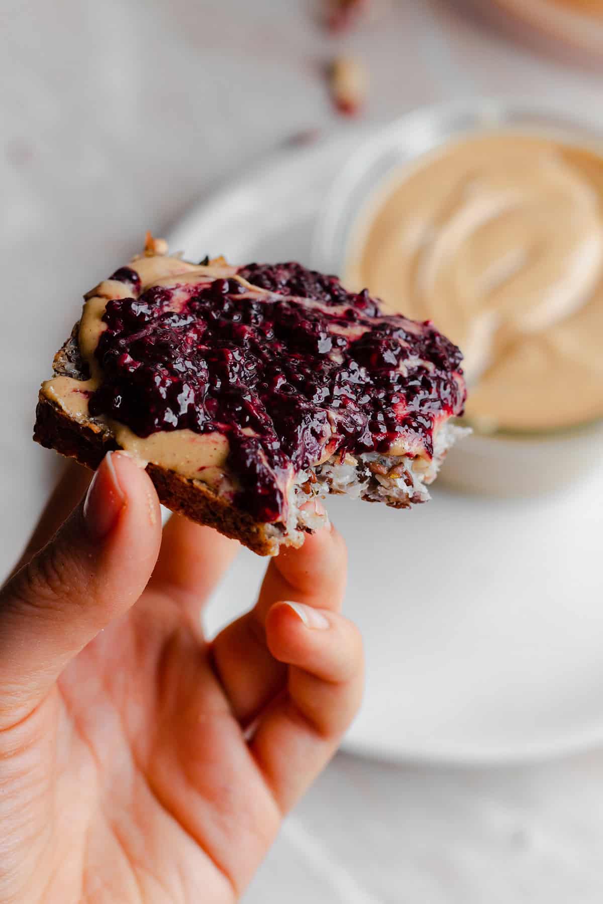 A hand holding a tost with peanut butter and berry chia jam