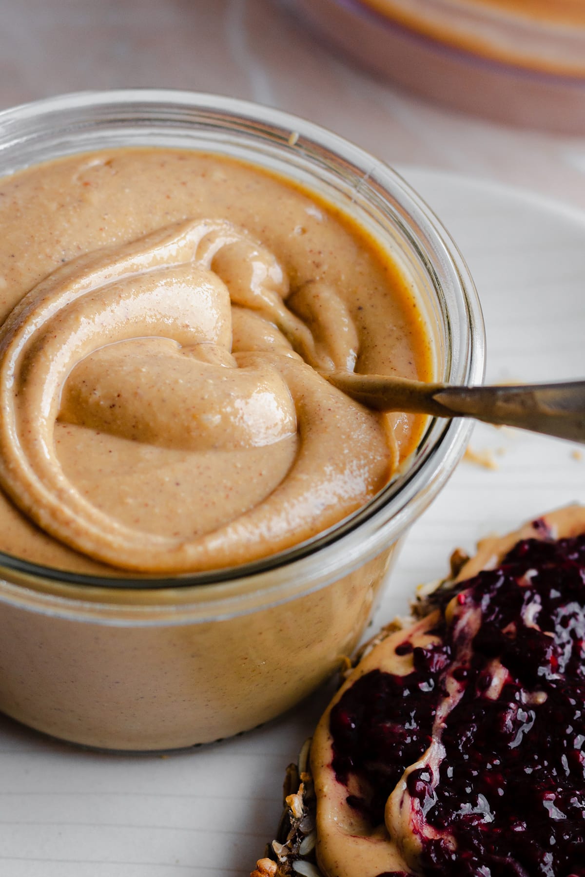 Wild Jungle Peanut Butter in a glass jar on a white plate. With a spoon in the jar.