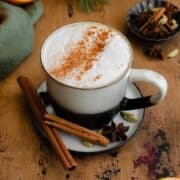 Overhead shot of Blood Orange Chai Tea Latte in a ceramic black and white mug. On a light wooden table with blood oranges around the mug.