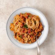 Creamy Sundried Tomato Pasta with Capers and Dill shown in a grey bowl with a silver fork in the bowl on the right side.