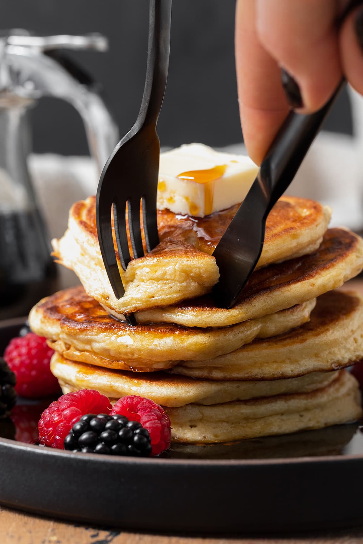 Greek Yogurt Pancakes stacked on a black plate. Black fork and knife cutting out a piece of the stack.