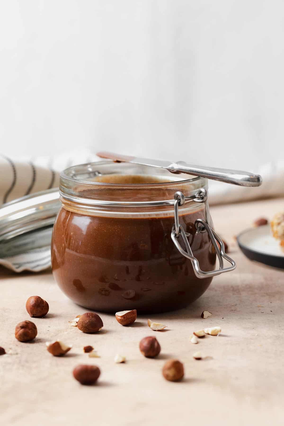 Homemade Nutella in a glass jar with a butterknife resting on the top.