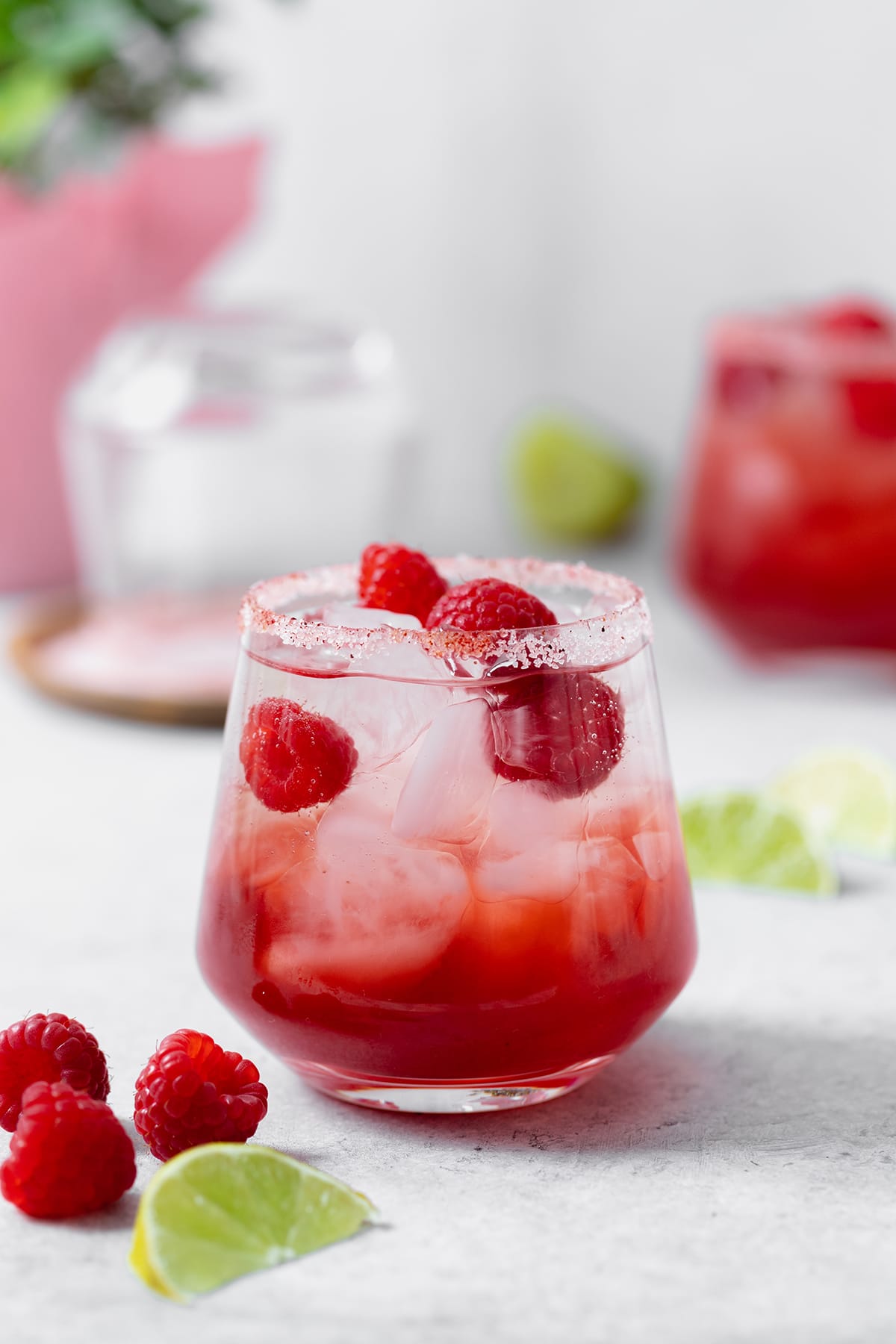 Raspberry margarita shown in a double old-fashioned glass with ice and fresh raspberries. On grey background.