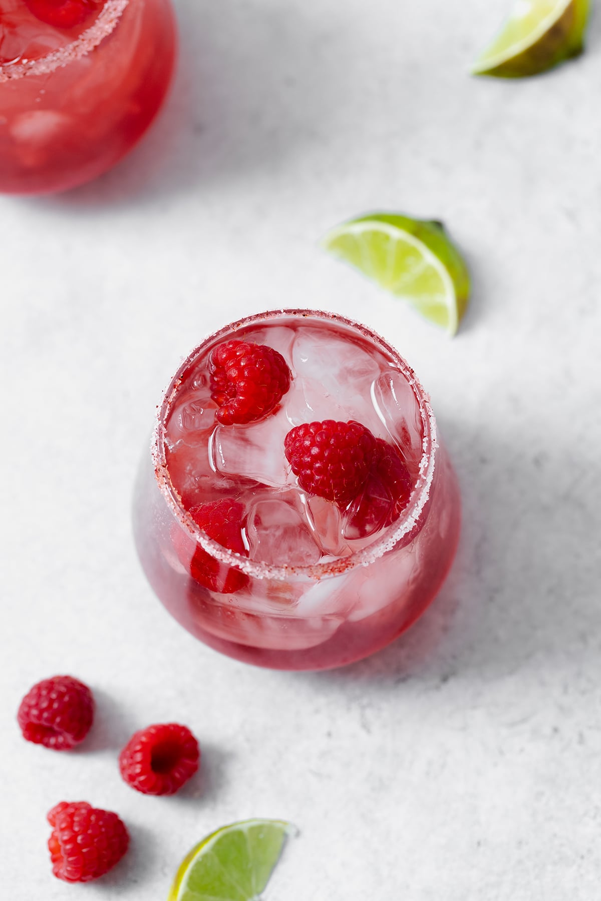 Raspberry margarita shown in a double old-fashioned glass with ice and fresh raspberries. On grey background. Shot from overhead