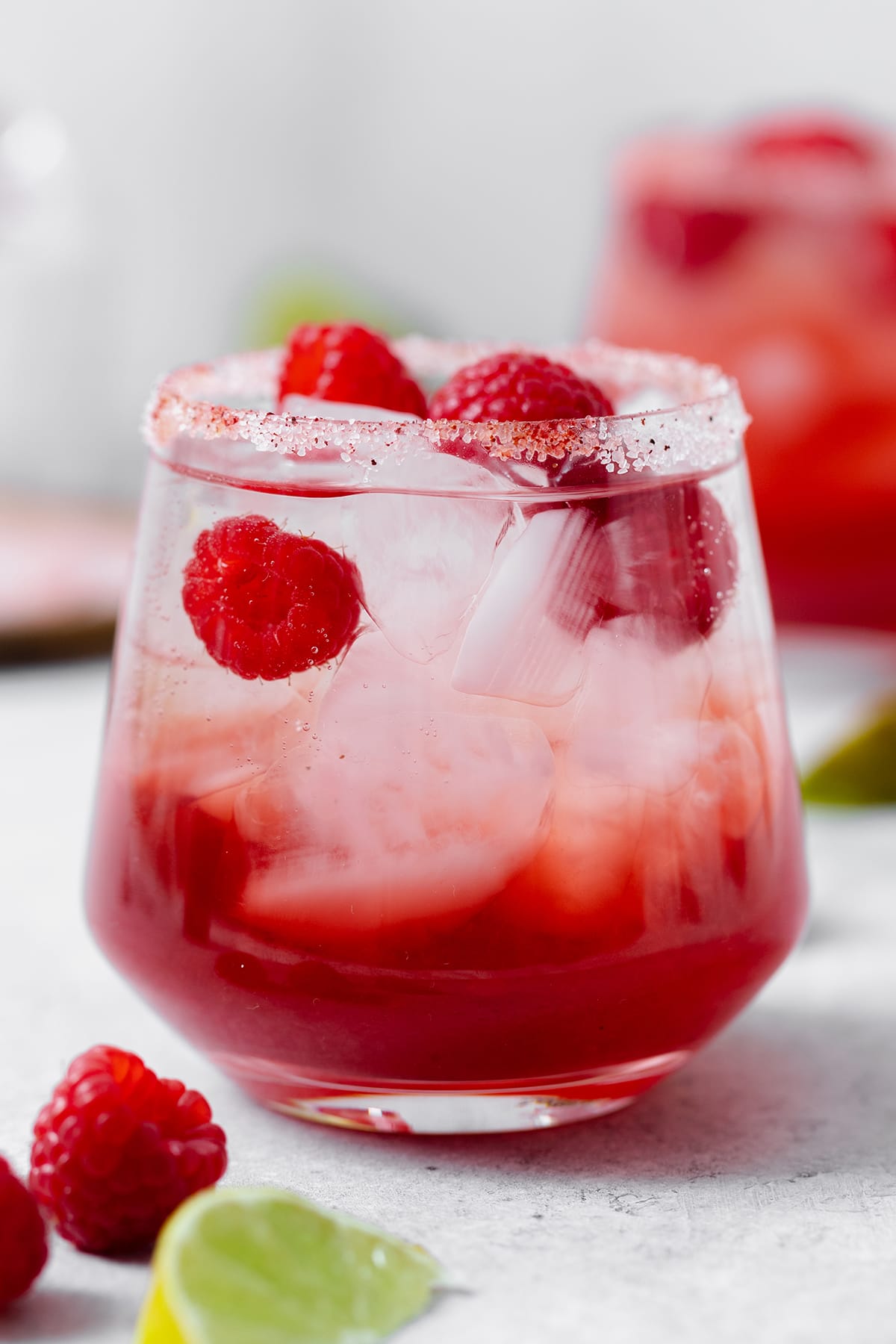 Raspberry margarita with sparkling water shown in a double old-fashioned glass with ice and fresh raspberries. On grey background.