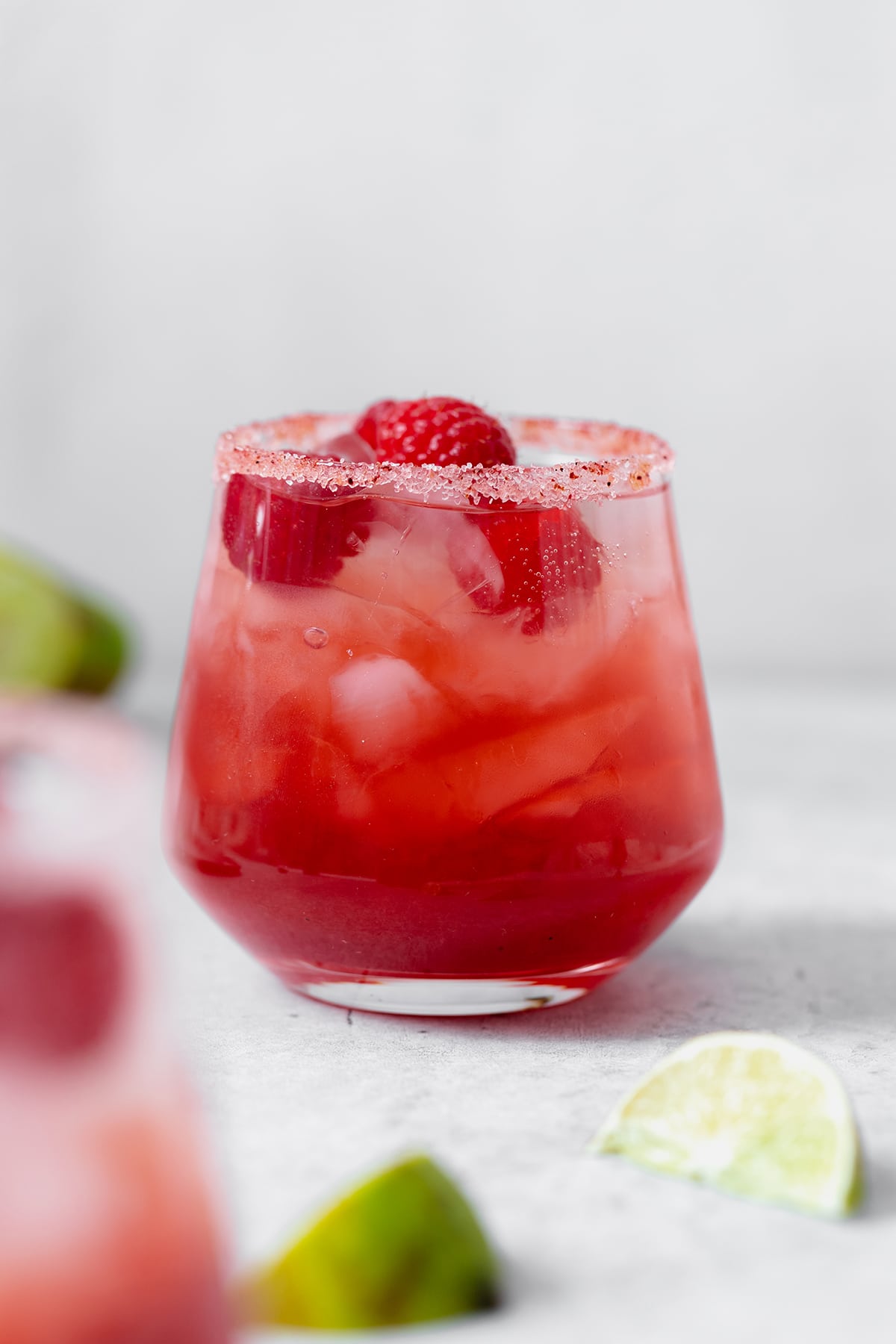 Bright pink Raspberry margarita shown in a double old-fashioned glass with ice and fresh raspberries. On grey background.