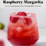 Raspberry margarita shown in a double old-fashioned glass with ice and fresh raspberries and lime wedges around the glass. On grey background.