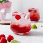 Raspberry margarita shown in a double old-fashioned glass with ice and fresh raspberries. On grey background.