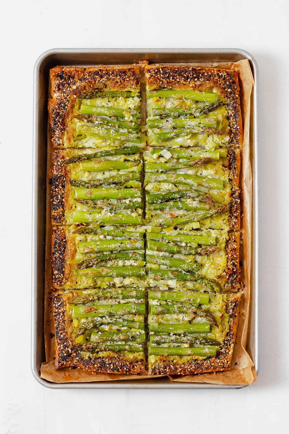 An asparagus tart on a baking sheet lined with parchment paper, cut into 8 squares.