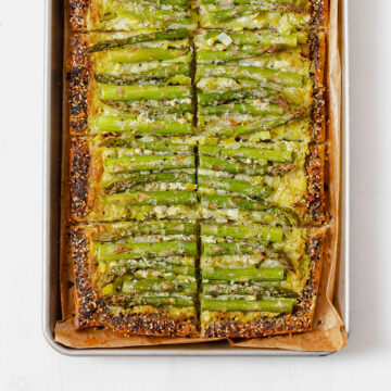 An asparagus tart on a baking sheet lined with parchment paper, cut into 8 squares.