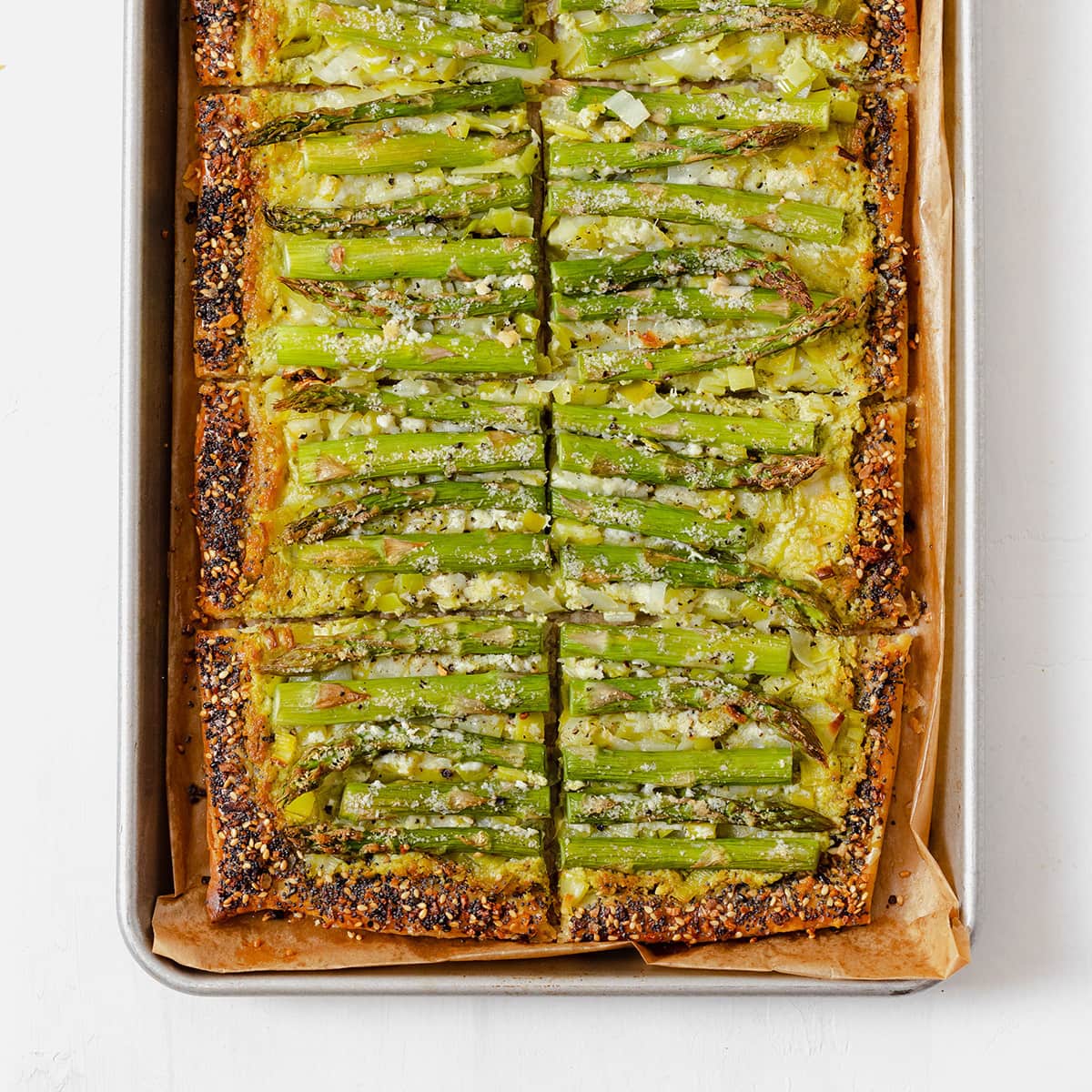 An asparagus tart on a baking sheet lined with parchment paper, cut into 8 squares.