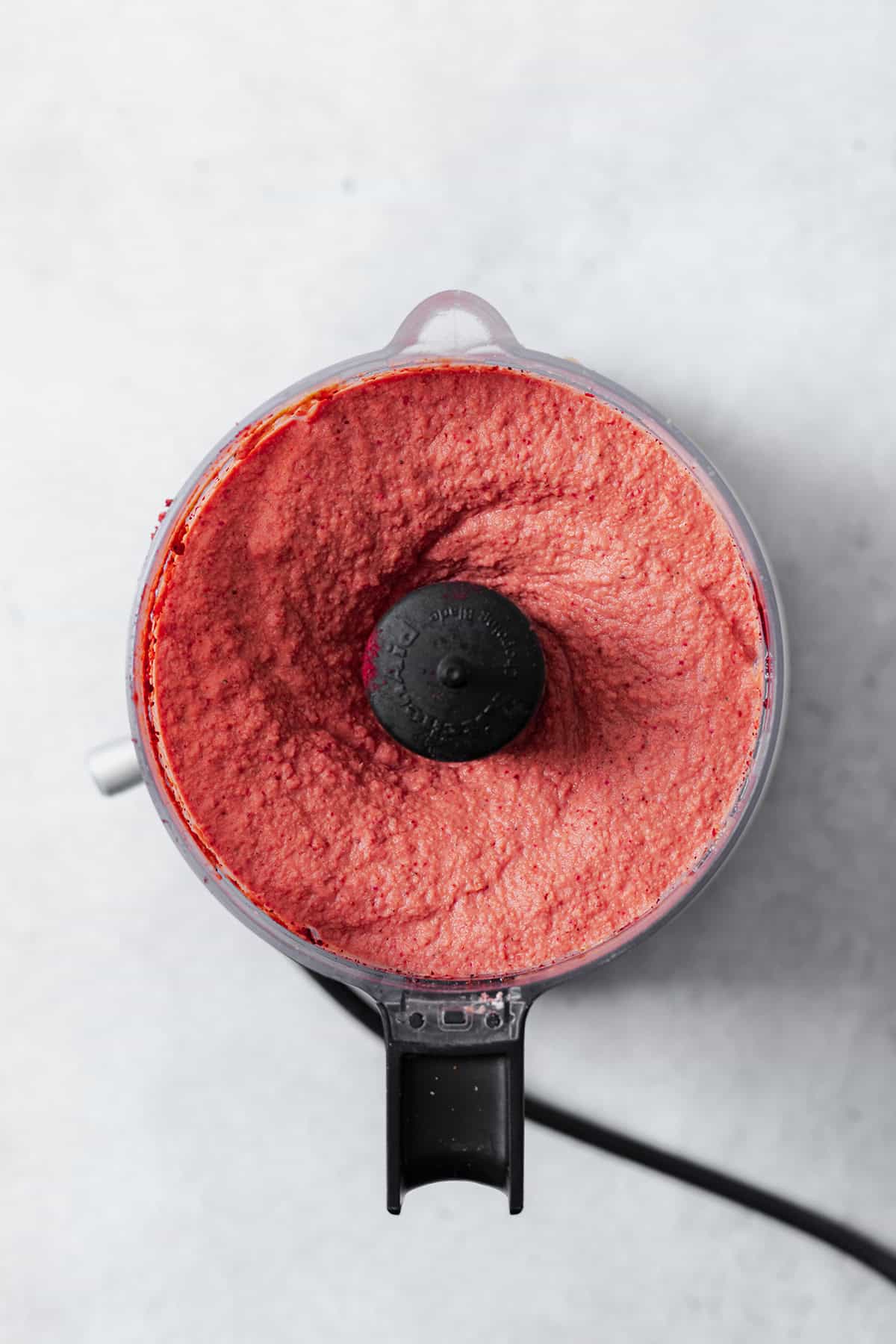 A photo of a small food processor full of the beet hummus after it's been blended.