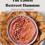 Beet hummus shown in a grey bowl on a grey plate surrounded by homemade pita chips. Grey background with a beige tea towel on the left of the bowl. Photo says "The Easiest Beetroot Hummus"