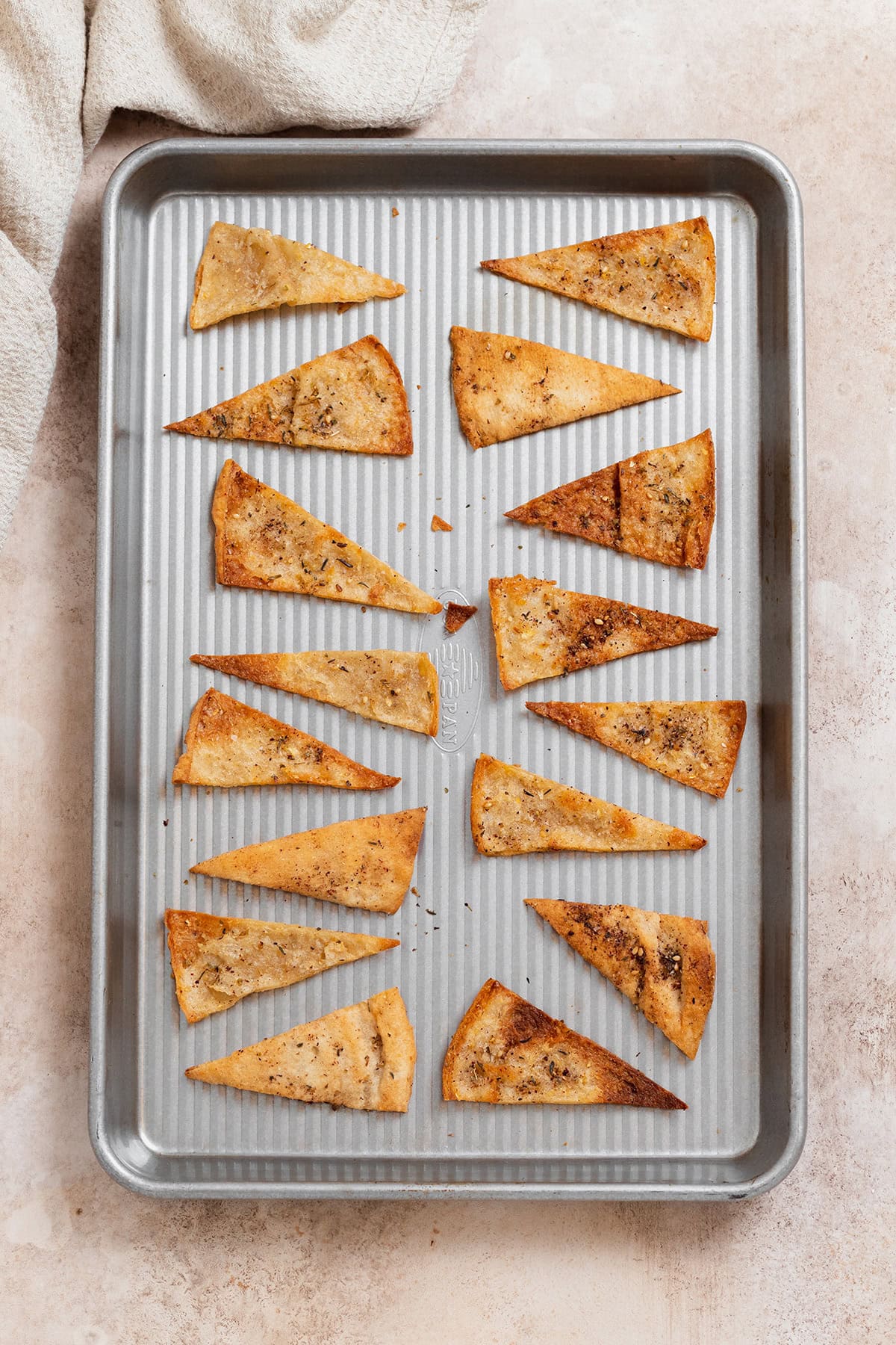 Homemade pita chips on a silver baking sheet.