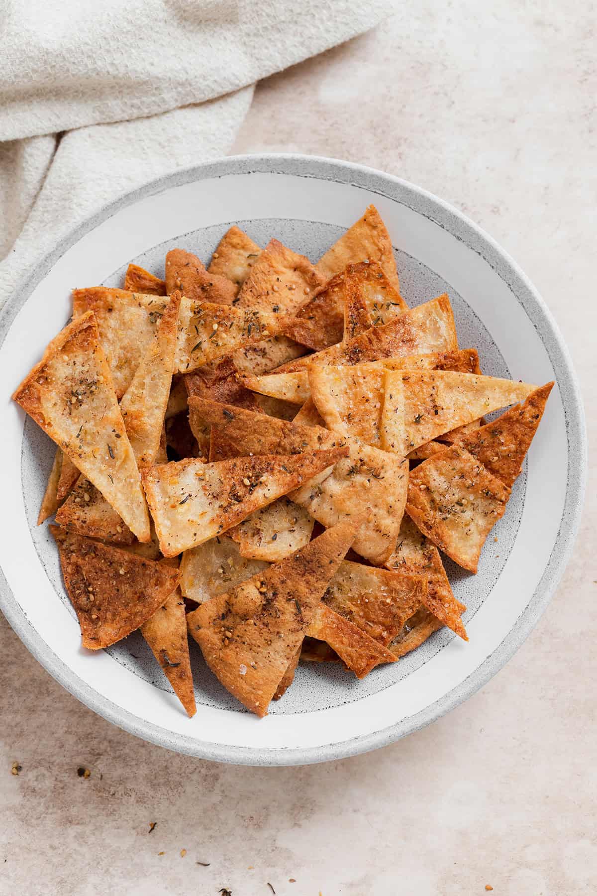 A close up photo of homemade pita chips in a grey bowl on a beige background.