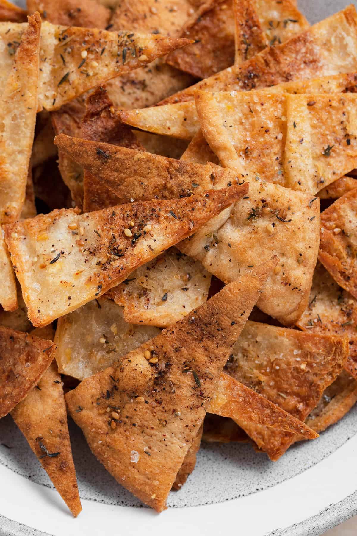 A close up photo of homemade pita chips in a grey bowl on a beige background.