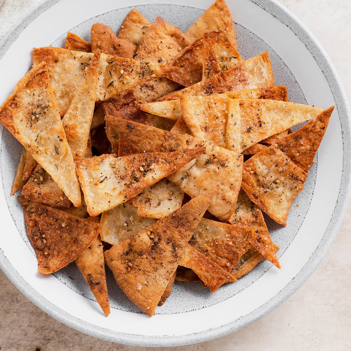 A close up photo of homemade pita chips in a grey bowl on a beige background.