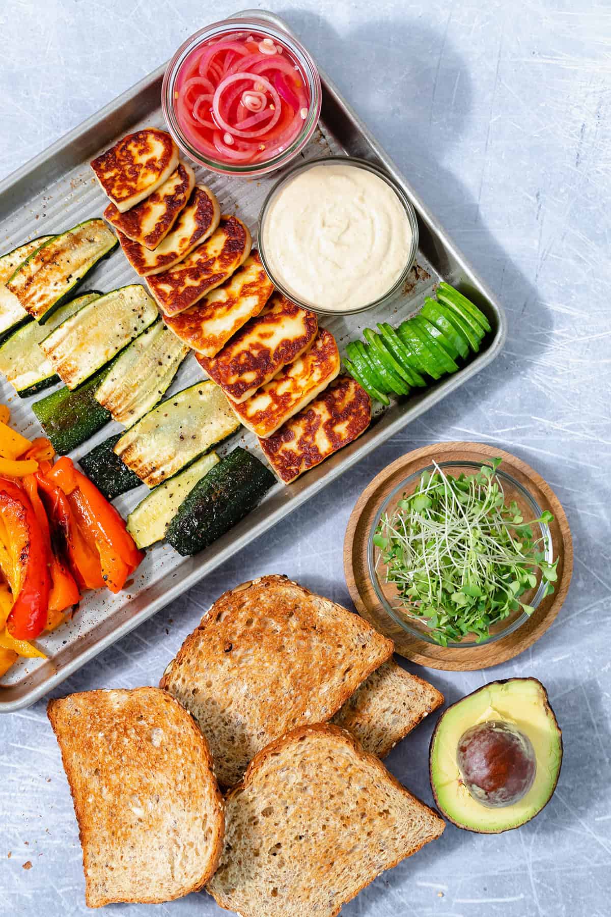 All the ingredients for halloumi sandwich all laid out on a baking sheet and a steel background.