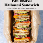 Halloumi sandwiches cut in half and arranged cut side up in a baking dish lined with parchment paper. Text overlay that says Pan-Seared Halloumi Sandwiches.