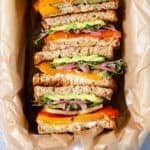 A square photo of halloumi sandwiches laid cut side in a dish lined with parchment paper.