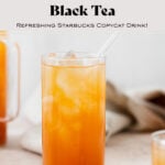 Iced Guava Black Tea shown in a tall glass with ice and a glass straw on beige background. More glasses and a jug full of iced tea partially in the frame on both left and right. Beige tea towel blurry in the background.