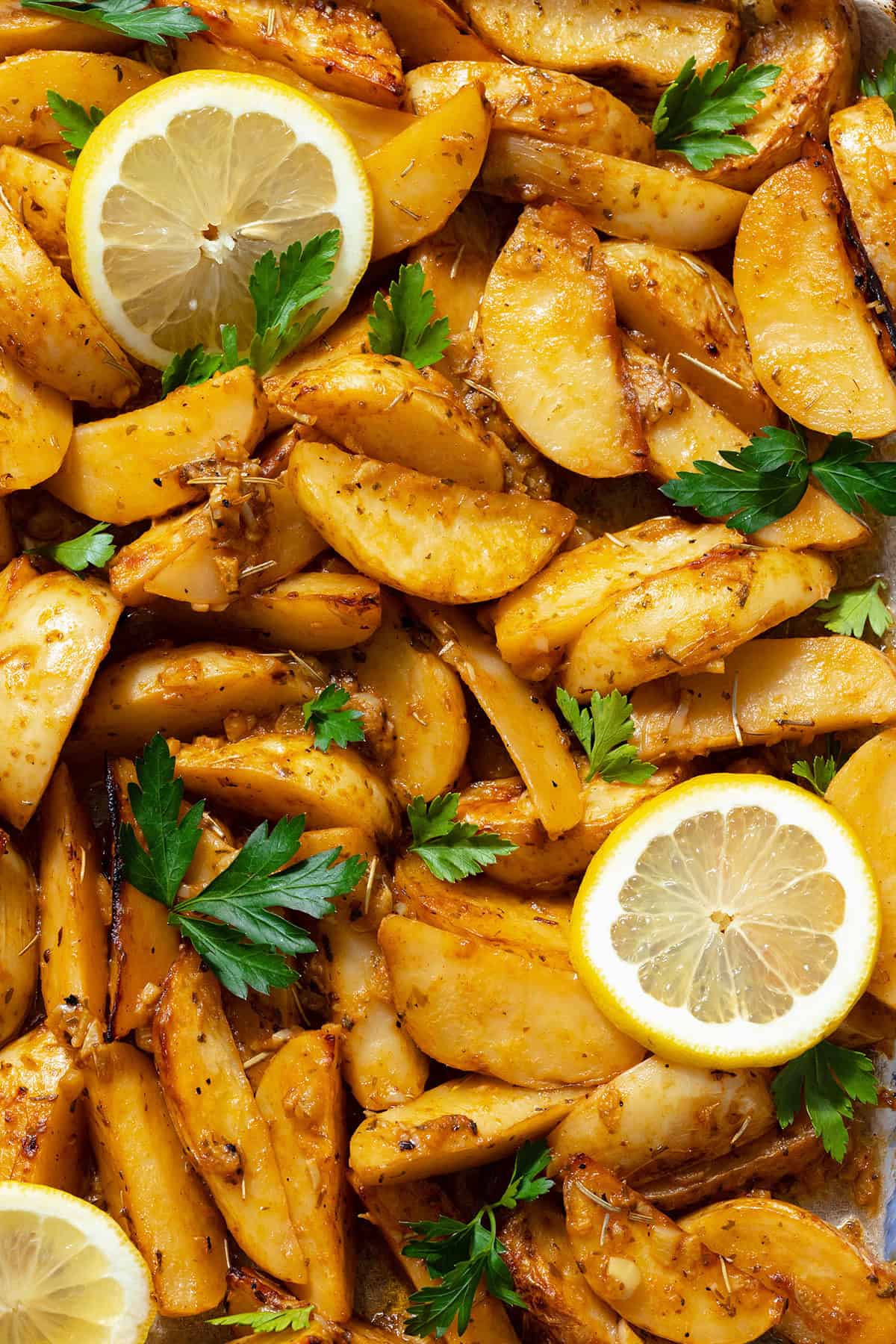 A close up photo of Mediterranean Potatoes garnished with three slice of lemon and chopped parsley.