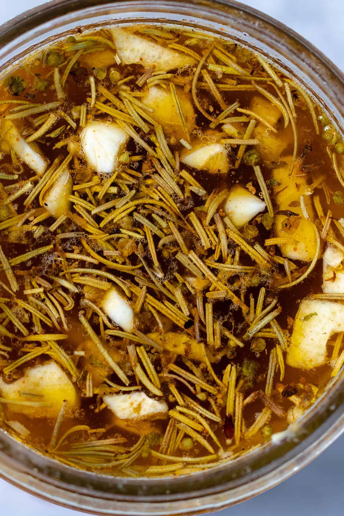 A close up of the sauce - olive oil, lemon juice, vegetable broth, herbs, and chopped garlic in a glass jar.