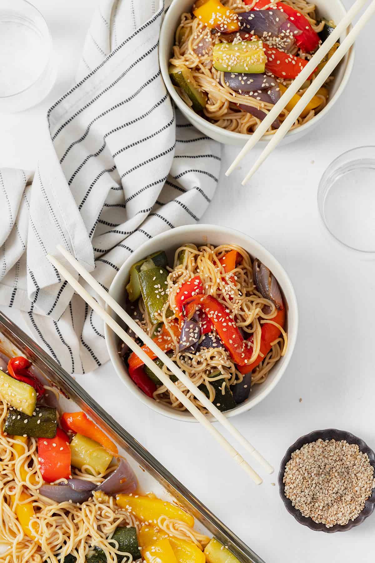 Gluten-free ramen noodle stir fry in two white bowls with chopsticks resting on the left side of the bowls. striped white and black napkin in the top left corner.