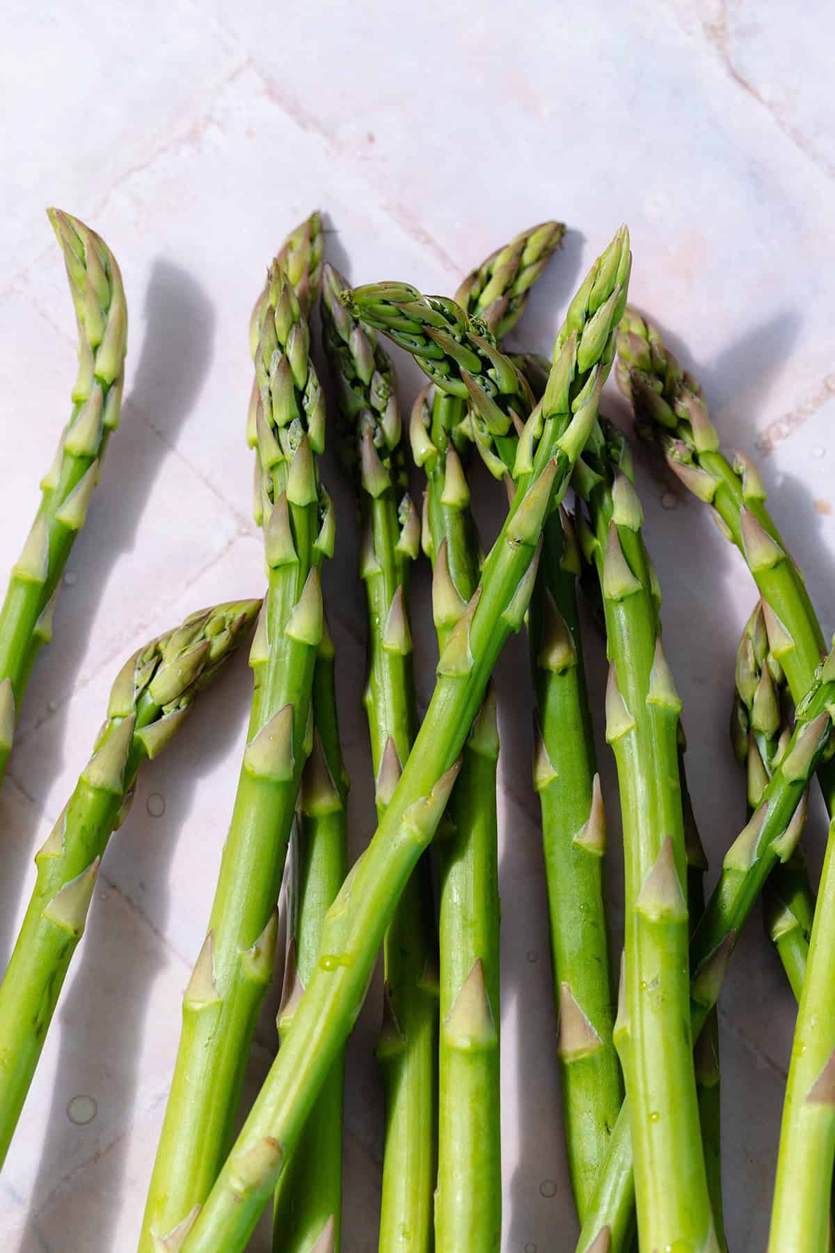 Fresh asparagus spears on pink tile background.