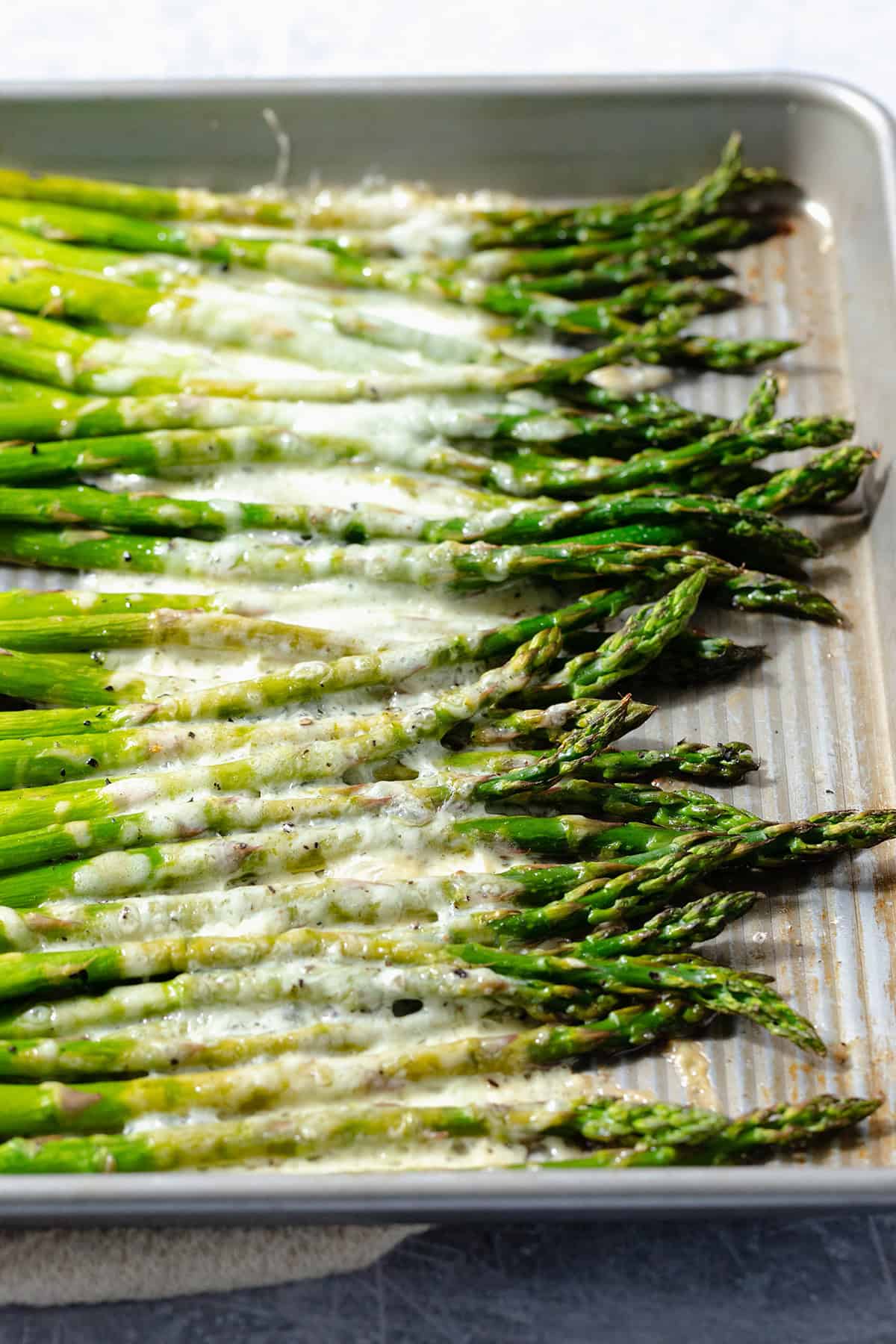 Roasted asparagus spears on a baking sheet with cheese sprinkled on that has melted in the oven.