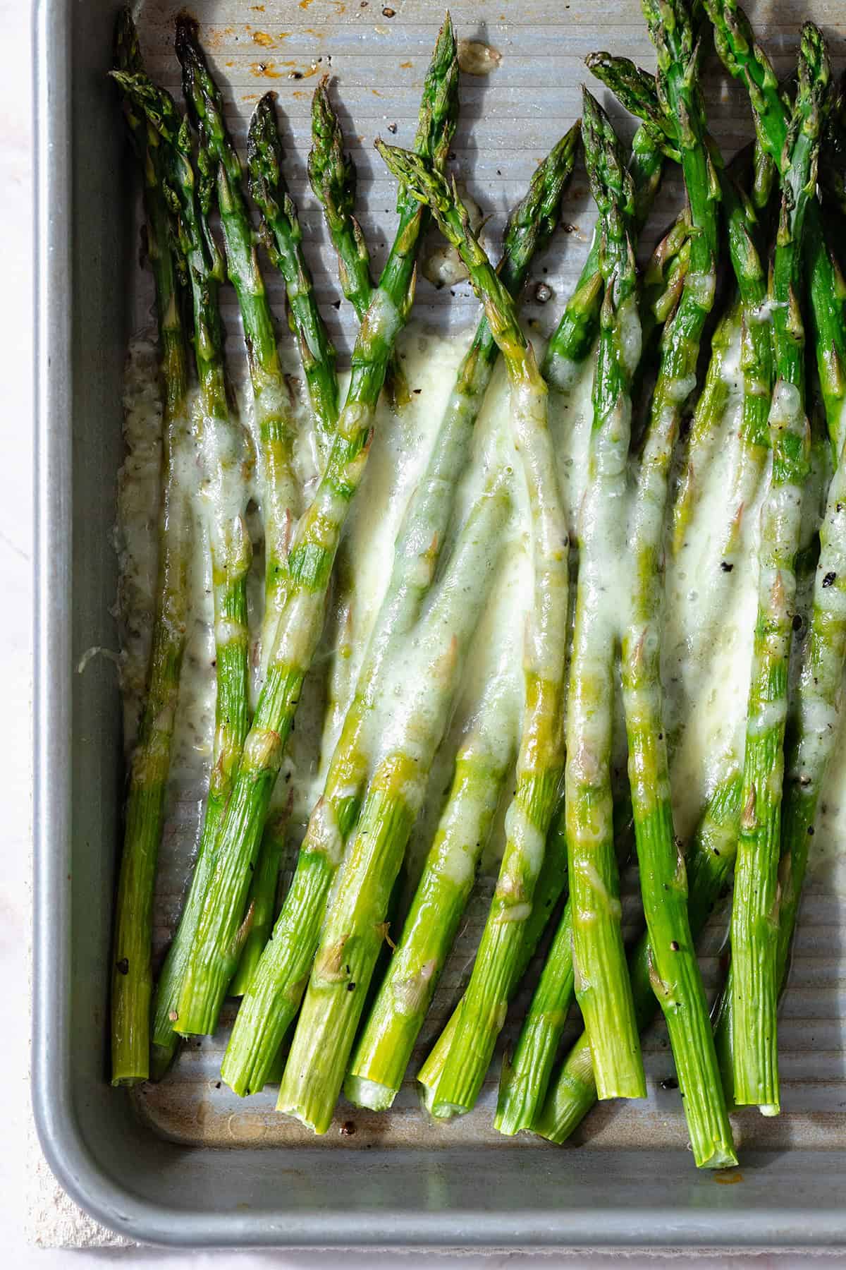 Baked asparagus spears on a sheet pan with cheese sprinkled on that has melted in the oven.