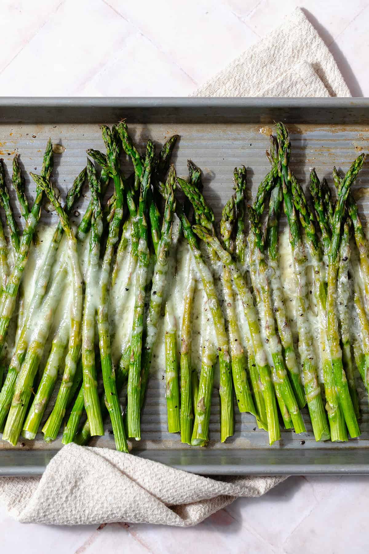 Baked asparagus spears on a sheet pan with cheese sprinkled on that has melted in the oven.