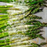 Baked asparagus spears on a sheet pan with cheese sprinkled on that has melted in the oven.