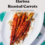 Harissa roasted carrots on a white serving platter with labneh spread under the carrots. Sprinkled with dukkah. Plate on a white and turquoise tile table.
