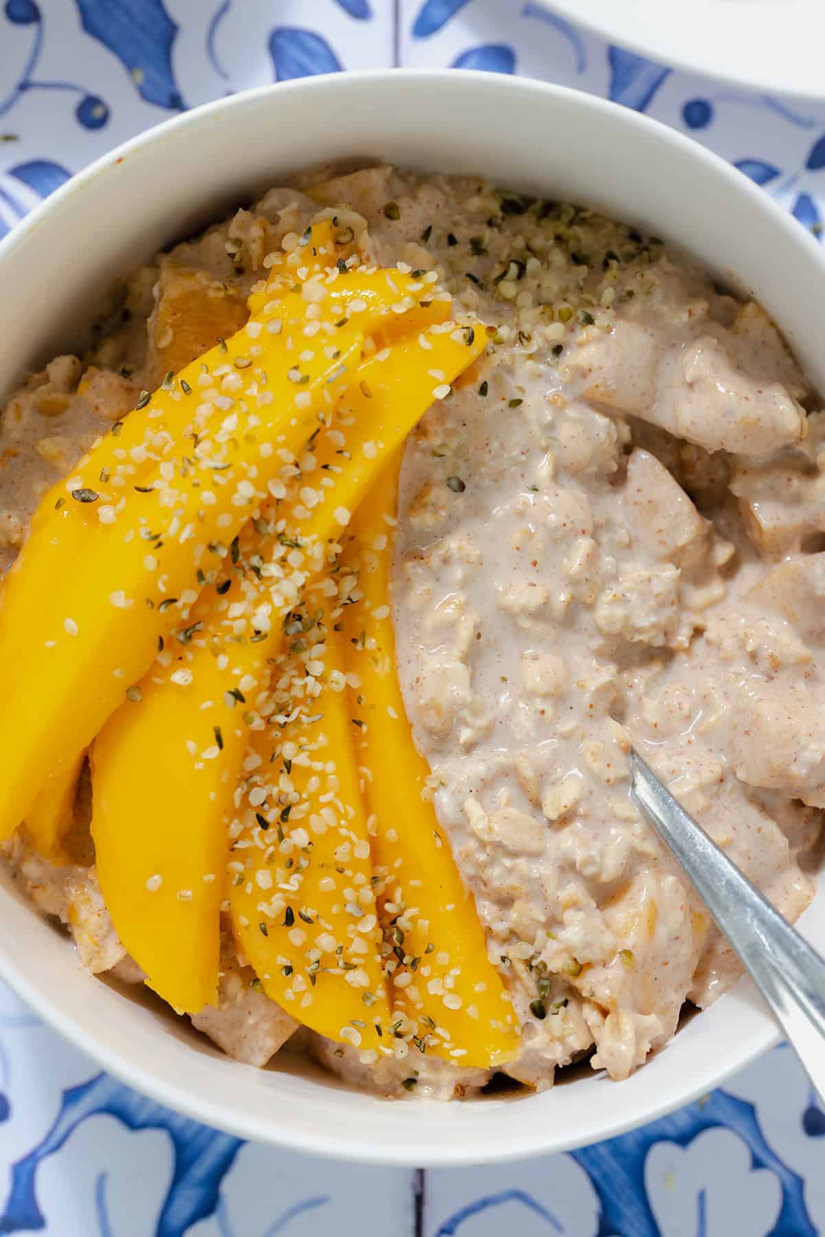 A close up photo of overnight oats with mango in a white bowl on a blue tile background.