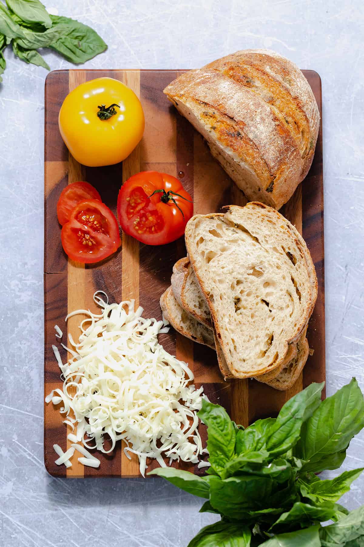 Ingredients for heirloom tomato grilled cheese layed out on a cutting board. There are tomatoes, shredded cheese, fresh basil, and sliced sourdough bread.