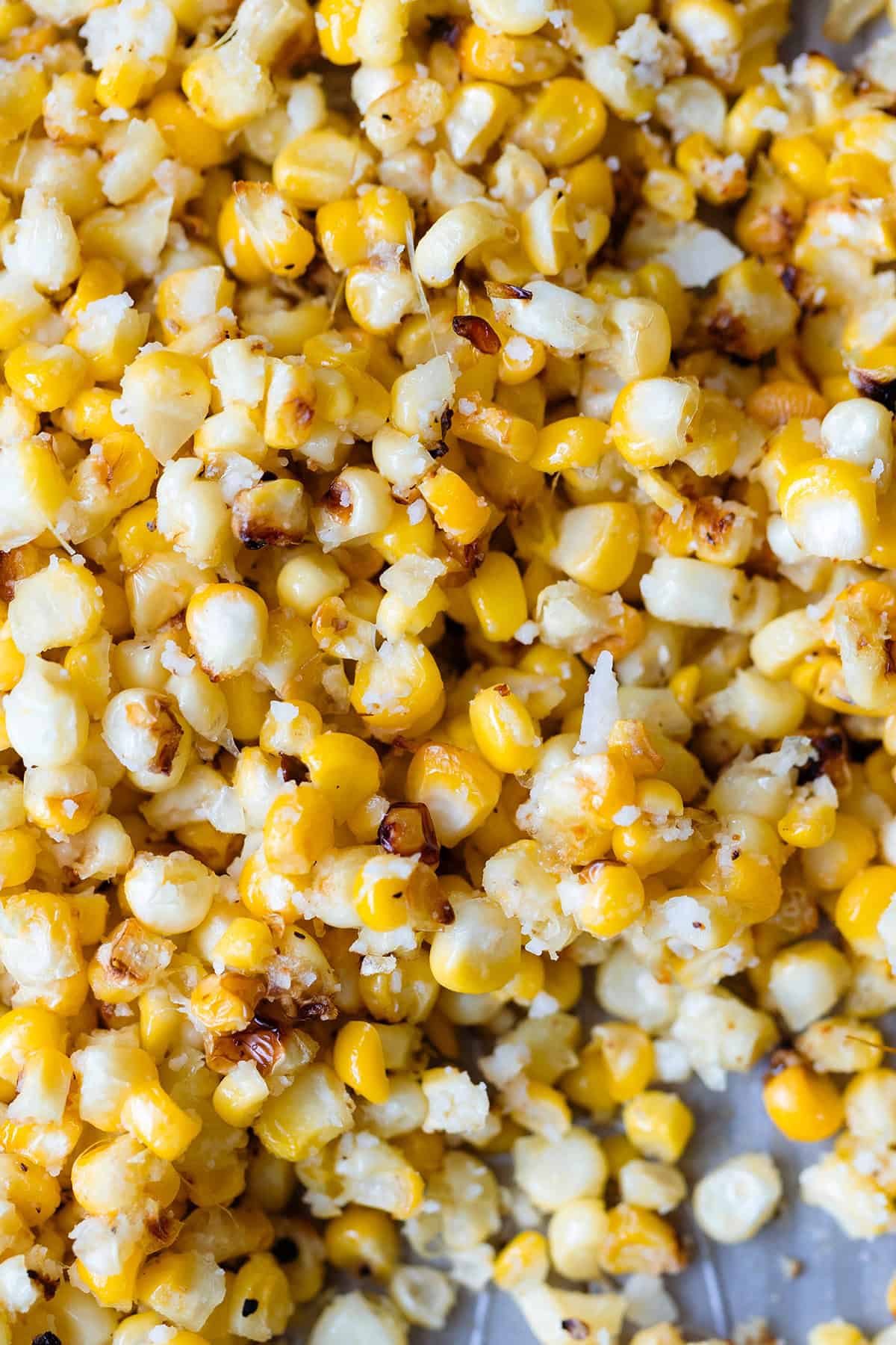 A close up of roasted corn kernels on a baking sheet, sprinkled with pecorino cheese