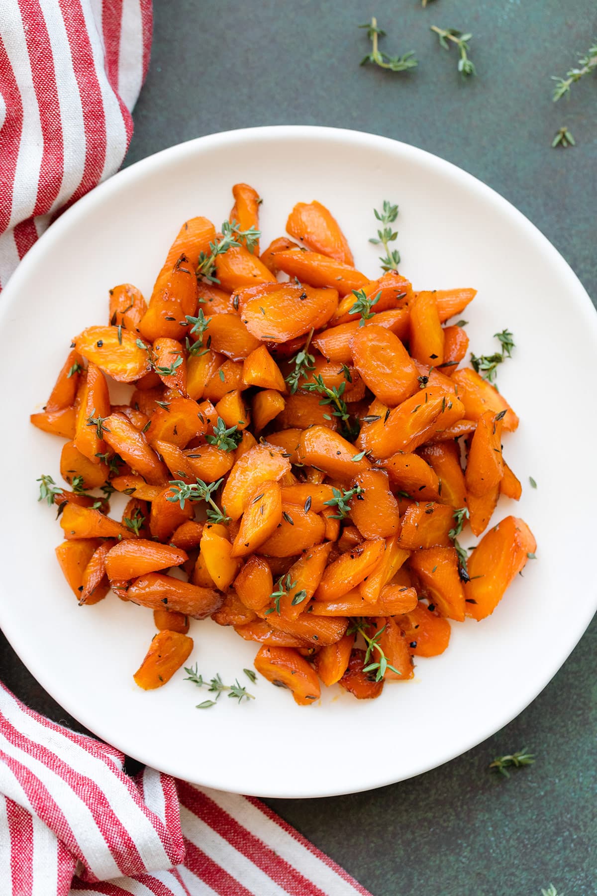 Roasted carrots garnished with fresh thyme on a white plate on a dark green background.