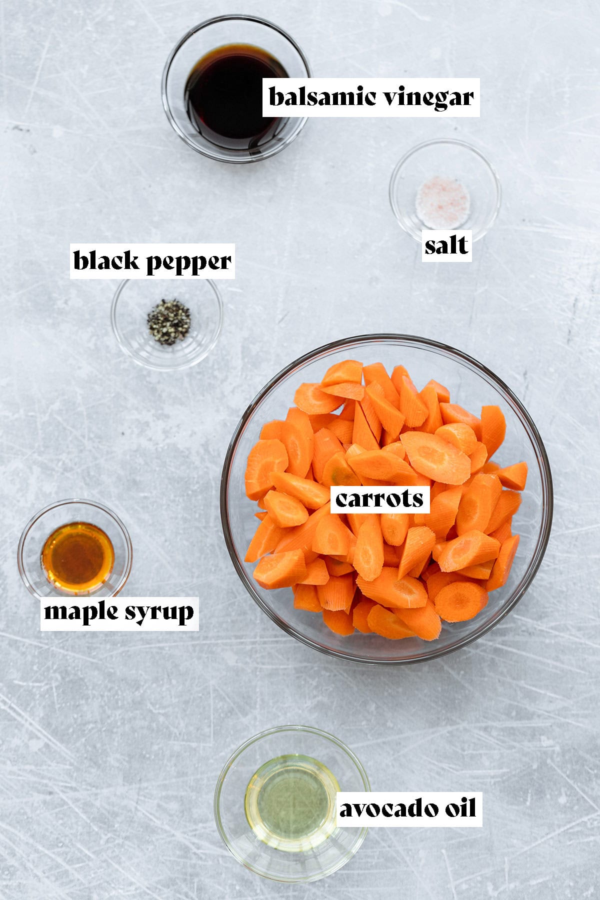 Ingredients needed to make balsamic roasted carrots on a light metal background.