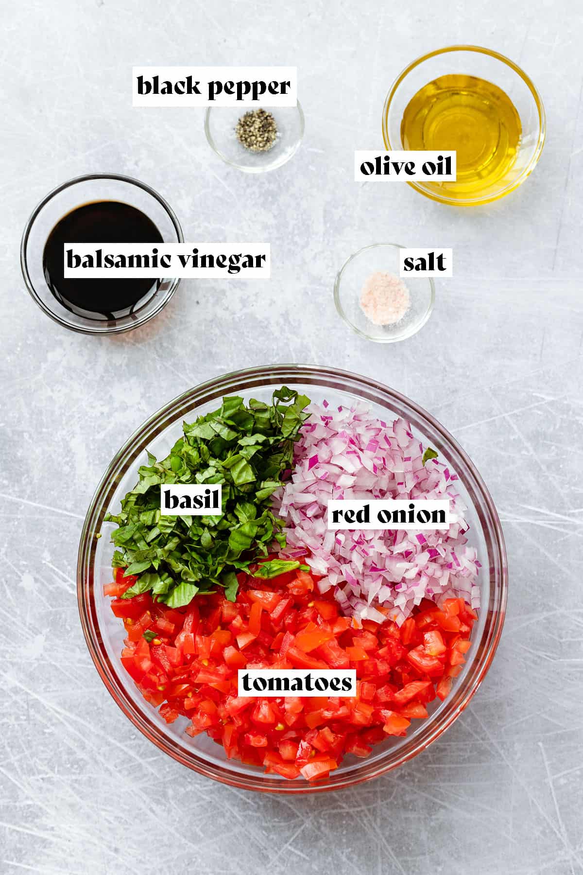 Ingredients for bruschetta with mozzarela laid out on a scratched metal background. Tomatoes, basil, red onion, olive oil, salt, black pepper, and balsamic vinegar.