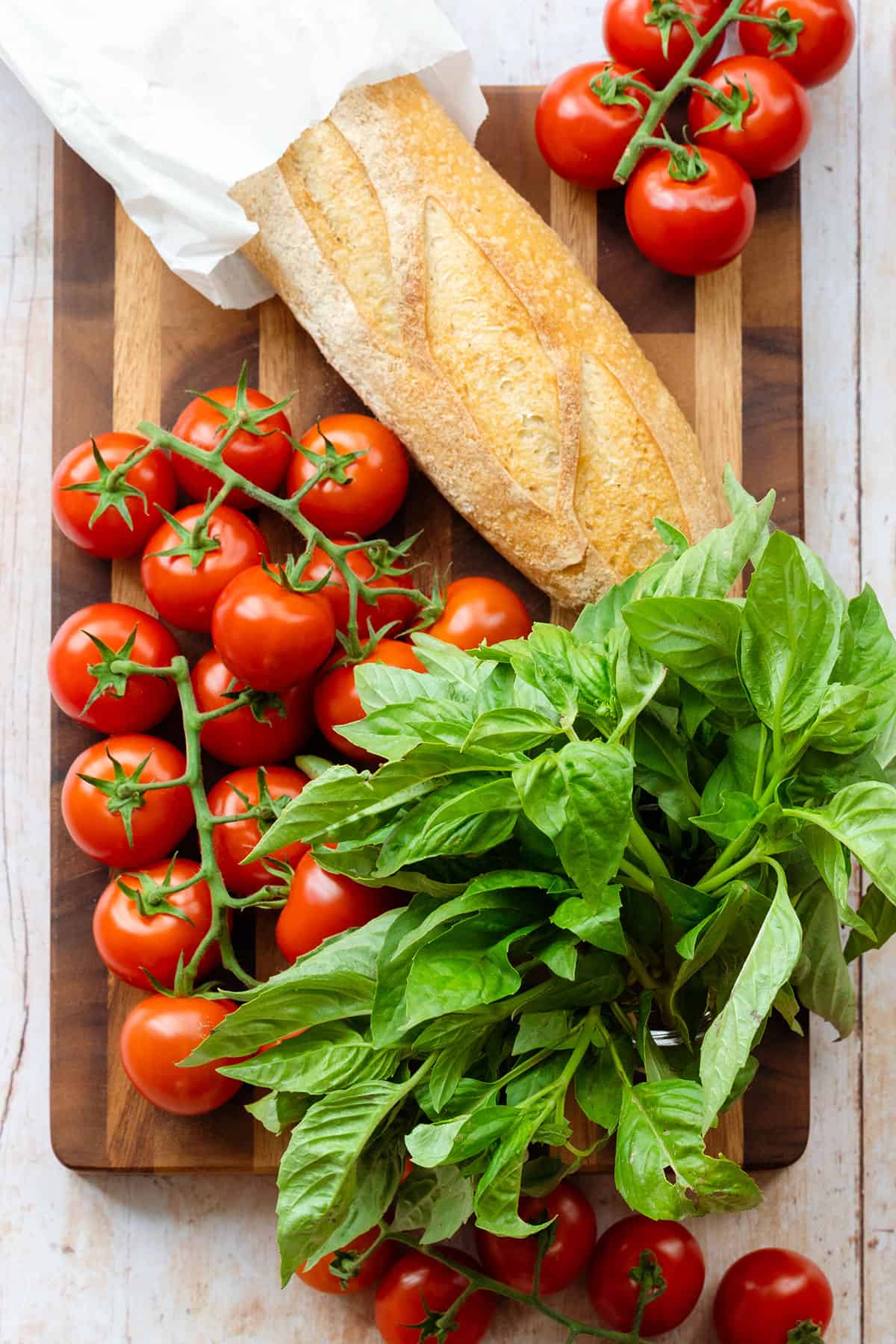 A fresh whole baguette, tomatoes on the wine, and fresh basil on a wooden cutting board.