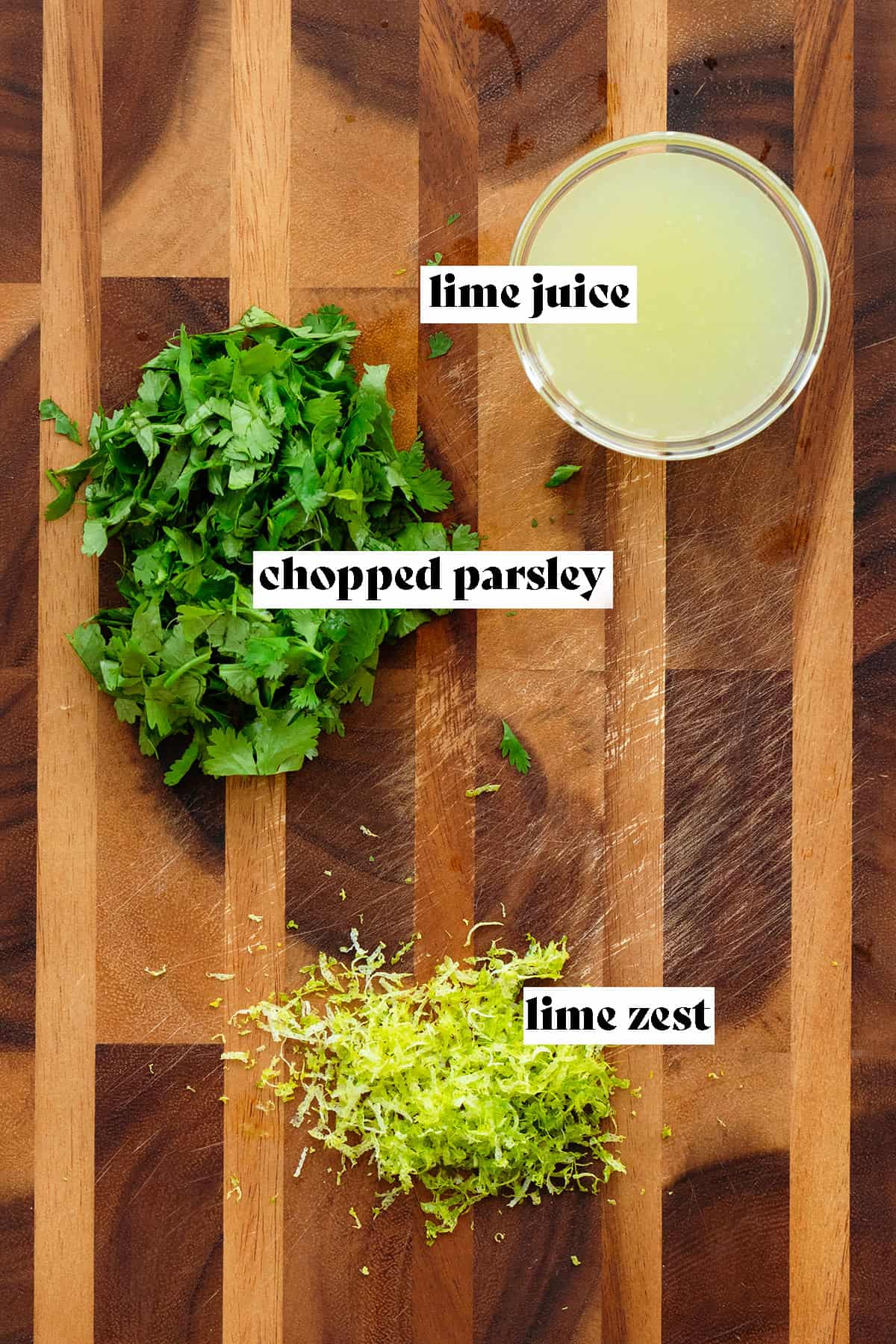 A photo of a wooden board with lime juice in a glass bowl in the top right, chopped fresh cilantro on the left, and fresh lime zest on the bottom middle.