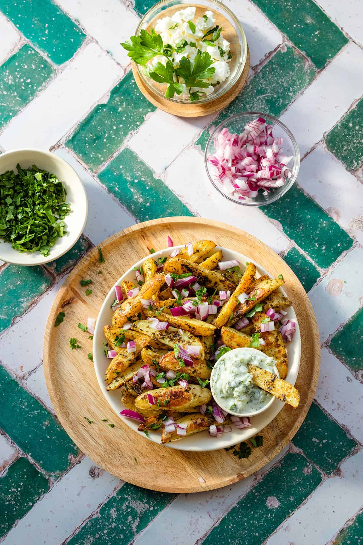 Greek fries with red onion and parsley on a white plate and a wooden serving plate.