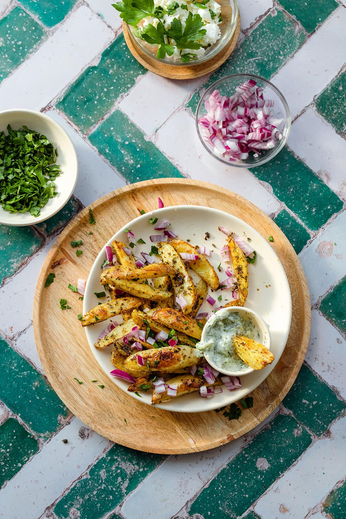Greek fries with red onion and parsley on a white plate and a wooden serving plate.
