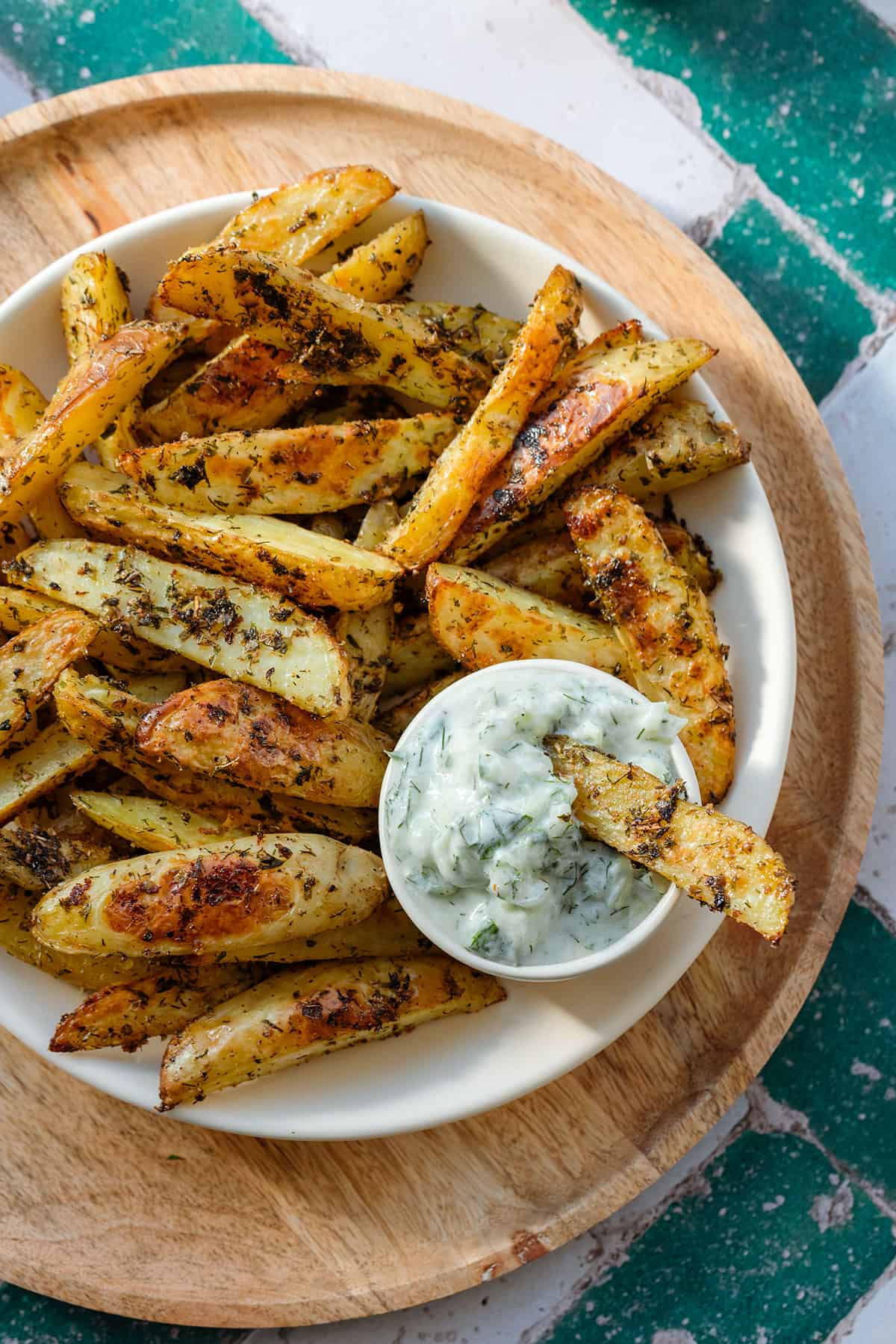 Fries in beige shallow bowl on a wooden serving plate on a green and white tile background.