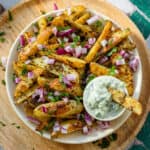 Greek fries with red onion and parsley on a white plate and a wooden serving plate.