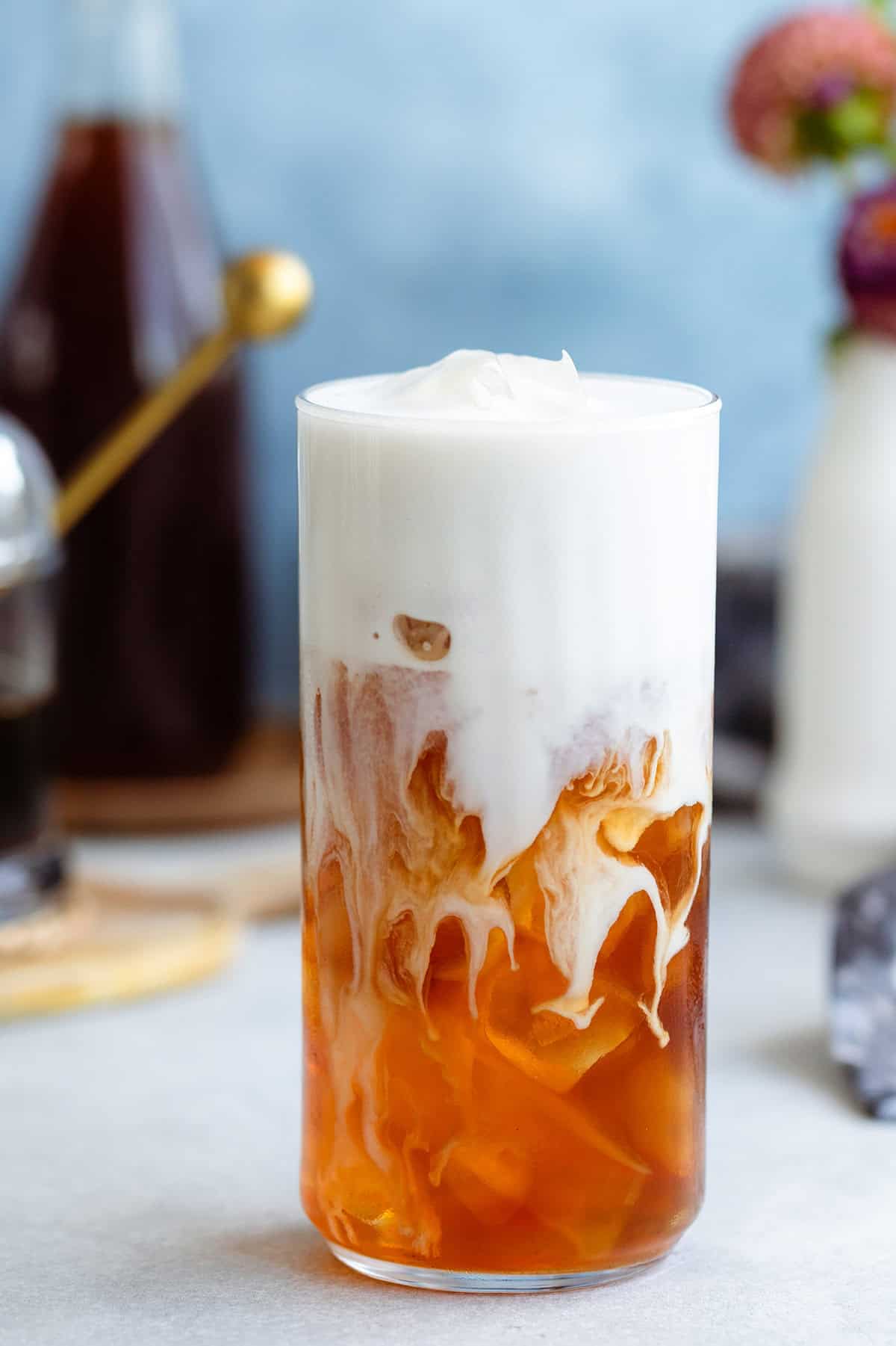 Earl grey in a tall glass with ice and frothy milk on top slowly blending together.